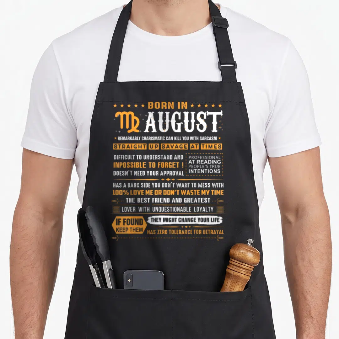 August virgo birthday apron - Orange and white typography listing Virgo traits like sarcasm and loyalty next — shown on a black cotton canvas apron against a white background