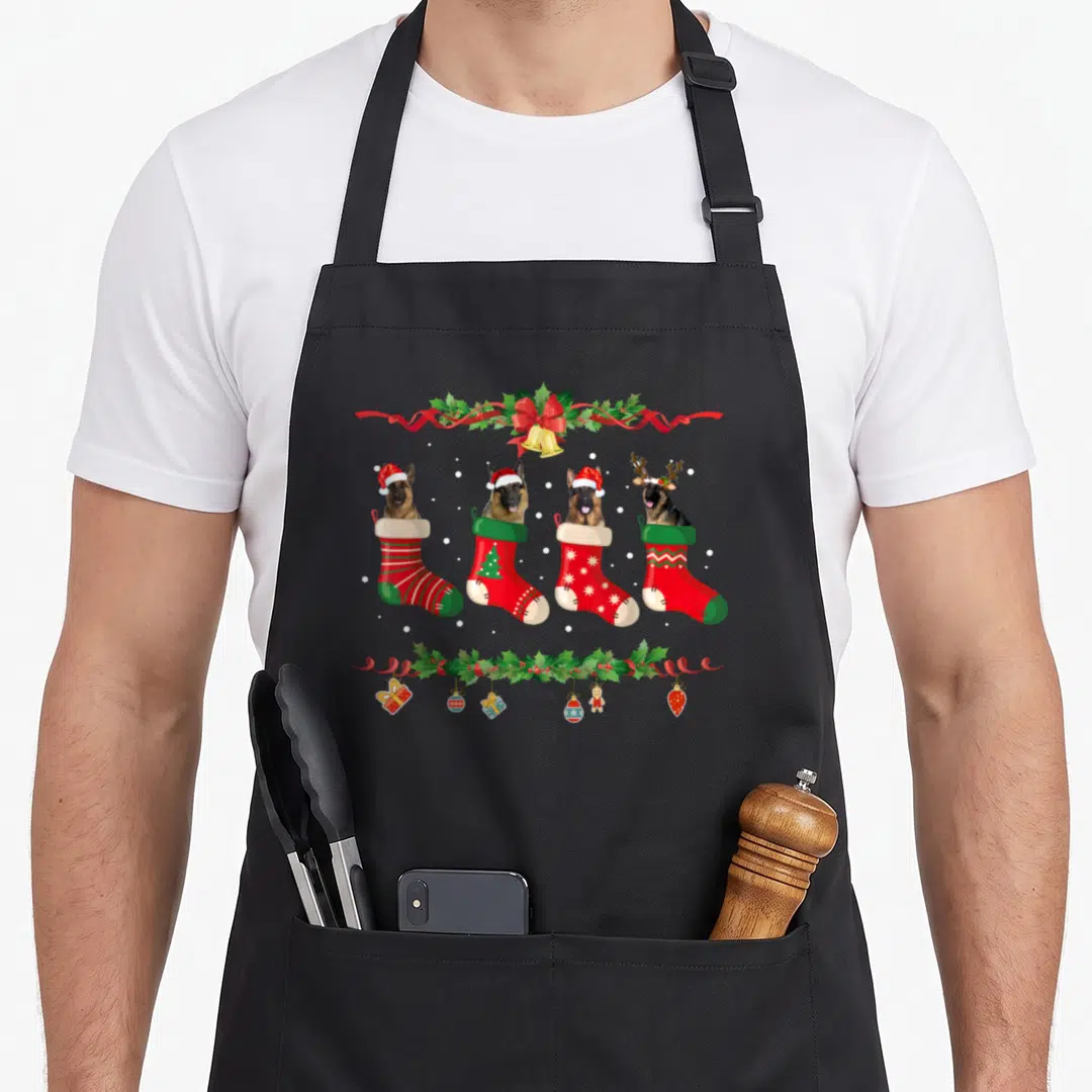 German christmas dog apron - Four German Shepherd dogs inside red and green Christmas stockings with holly garlands — shown on a black cotton canvas apron against a white background
