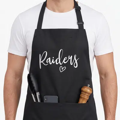 Raider sports team aprons - White cursive Raiders text with a heart symbol below — shown on a black cotton canvas apron against a white background