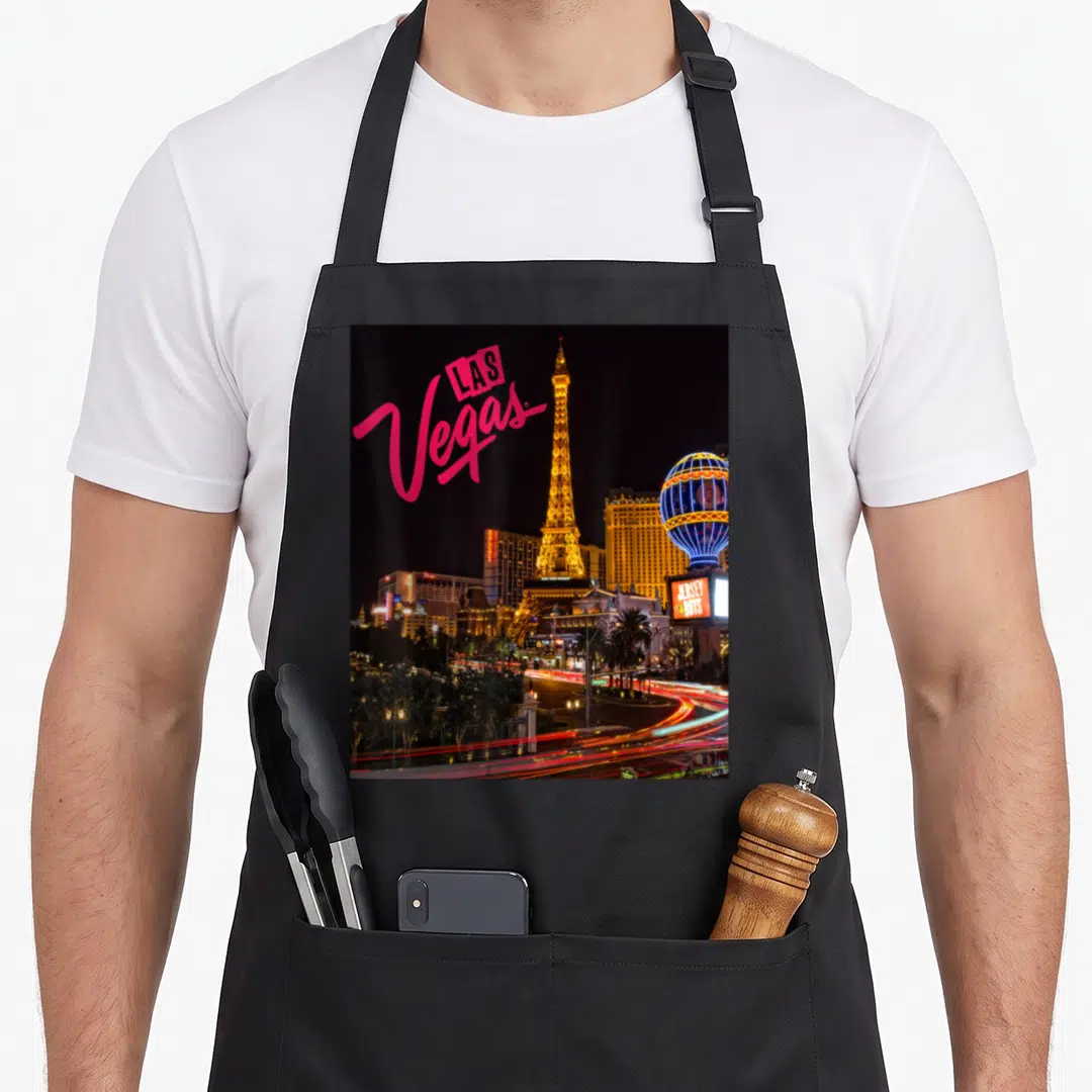 Strip las vegas apron - Pink LAS Vegas text over golden Eiffel Tower replica and blue hot air balloon at night — shown on a black cotton canvas apron against a white background