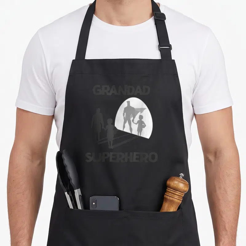 Superhero grandad aprons - Grandad Superhero silhouette casting a caped shadow on grey background — shown on a black cotton canvas apron against a white background