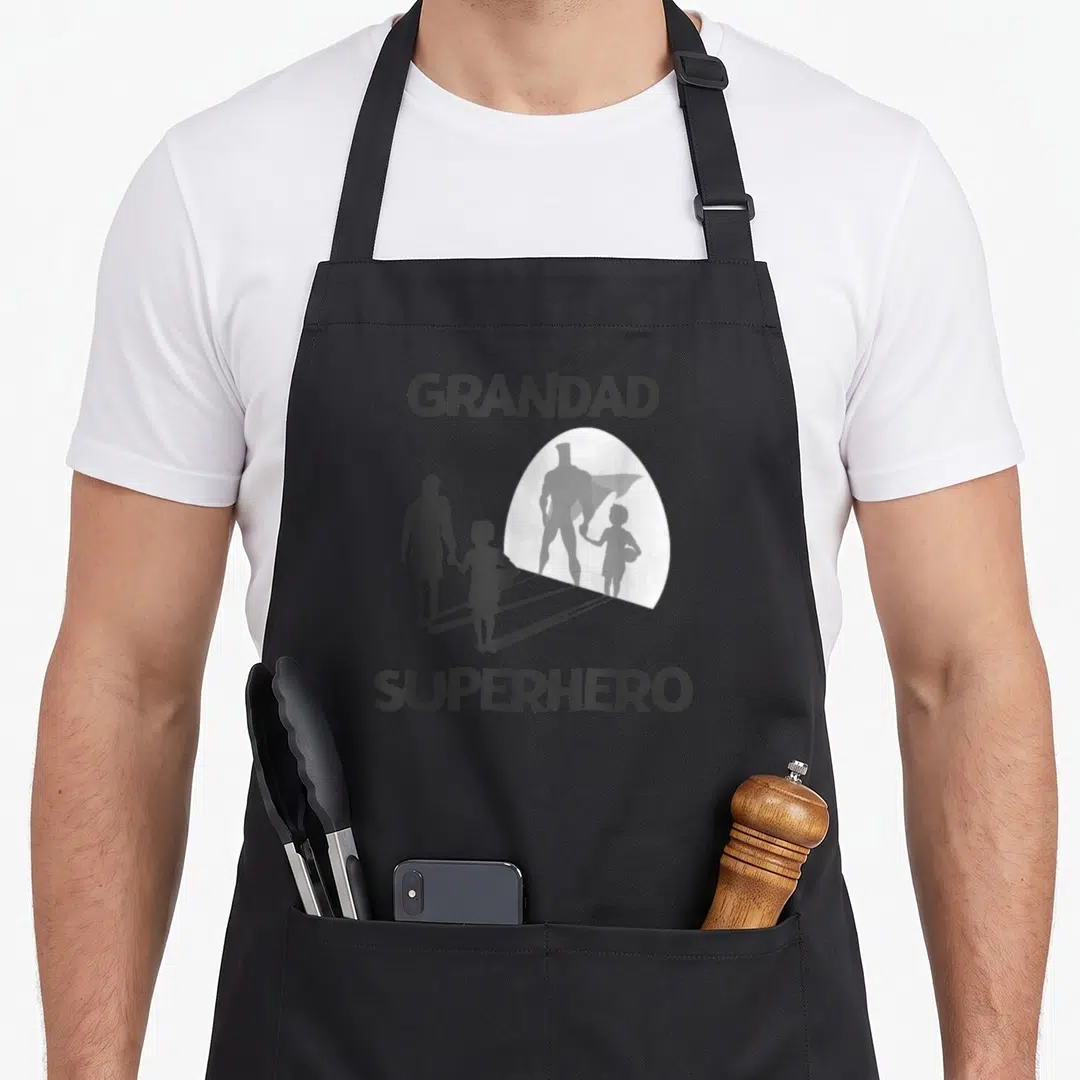 Superhero grandad aprons - Grandad Superhero silhouette casting a caped shadow on grey background — shown on a black cotton canvas apron against a white background