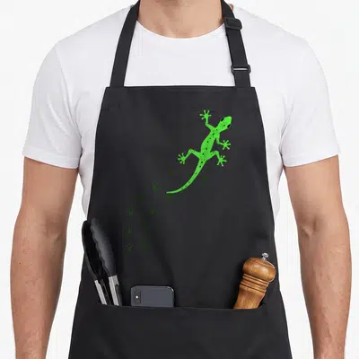 Gecko animal apron - Green cartoon lizard with dark green footprint trail on grey background — shown on a black cotton canvas apron against a white background