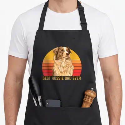 Papa australian aprons - Realistic Australian Shepherd on retro sunset circle with horizontal stripes and text BEST — shown on a black cotton canvas apron against a white background
