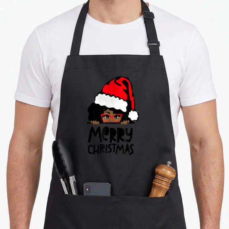 Melanin mrs apron - Woman in red Santa hat peeking over line above stacked Merry Christmas text in cartoon style — shown on a black cotton canvas apron against a white background