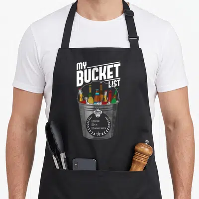 Beer bucket apron - Grey bucket with ice, colorful bottles, and My Bucket List checklist reading Beer Ice More Beer — shown on a black cotton canvas apron against a white background