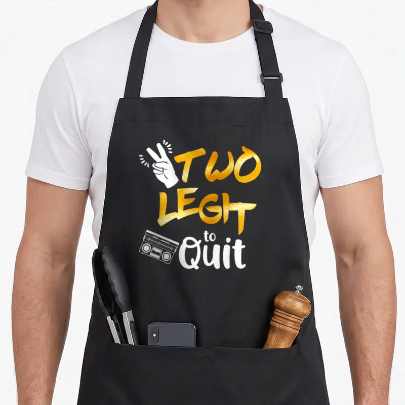 Hip 2nd apron - Gold TWO LEGIT to Quit text with white hand and boombox graphic — shown on a black cotton canvas apron against a white background