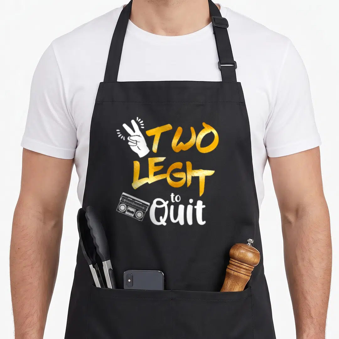 Hip 2nd apron - Gold TWO LEGIT to Quit text with white hand and boombox graphic — shown on a black cotton canvas apron against a white background