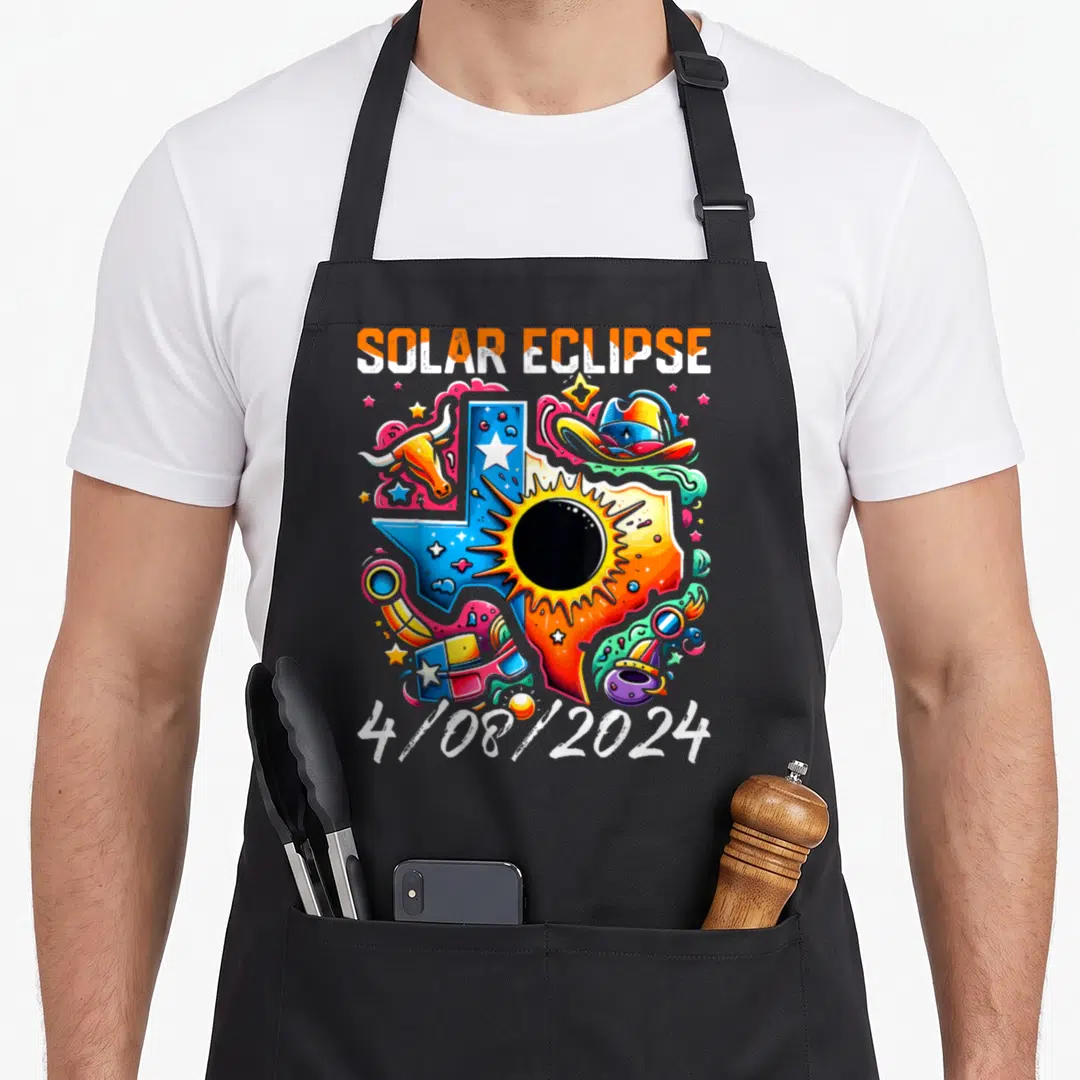 Eclipse solar texas apron - SOLAR ECLIPSE 4/08/2024 Texas map cartoon with longhorn skull cowboy hat abstract shapes — shown on a black cotton canvas apron against a white background