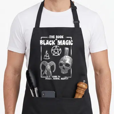 Alt gothic apron - White distressed text The Book of Black Magic Guide to Money Power Respect with skull pentagram — shown on a black cotton canvas apron against a white background