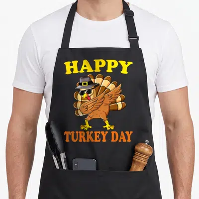Turkey pilgrim thanksgiving day aprons - Cartoon turkey in sunglasses and pilgrim hat between HAPPY and TURKEY DAY text — shown on a black cotton canvas apron against a white background