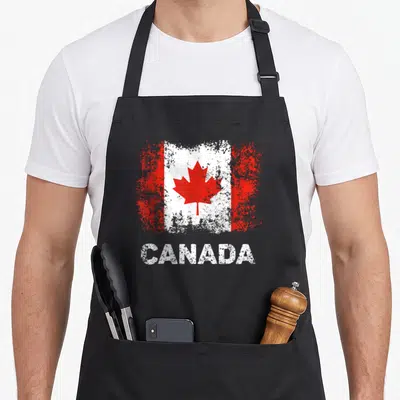 Canada patriotic apron - Distressed red white Canadian flag above white CANADA text — shown on a black cotton canvas apron against a white background
