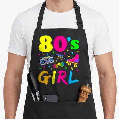 Costume birthday apron - 80s GIRL text with boombox, cassette, glasses, skate, stars, and lightning bolts in pink — shown on a black cotton canvas apron against a white background