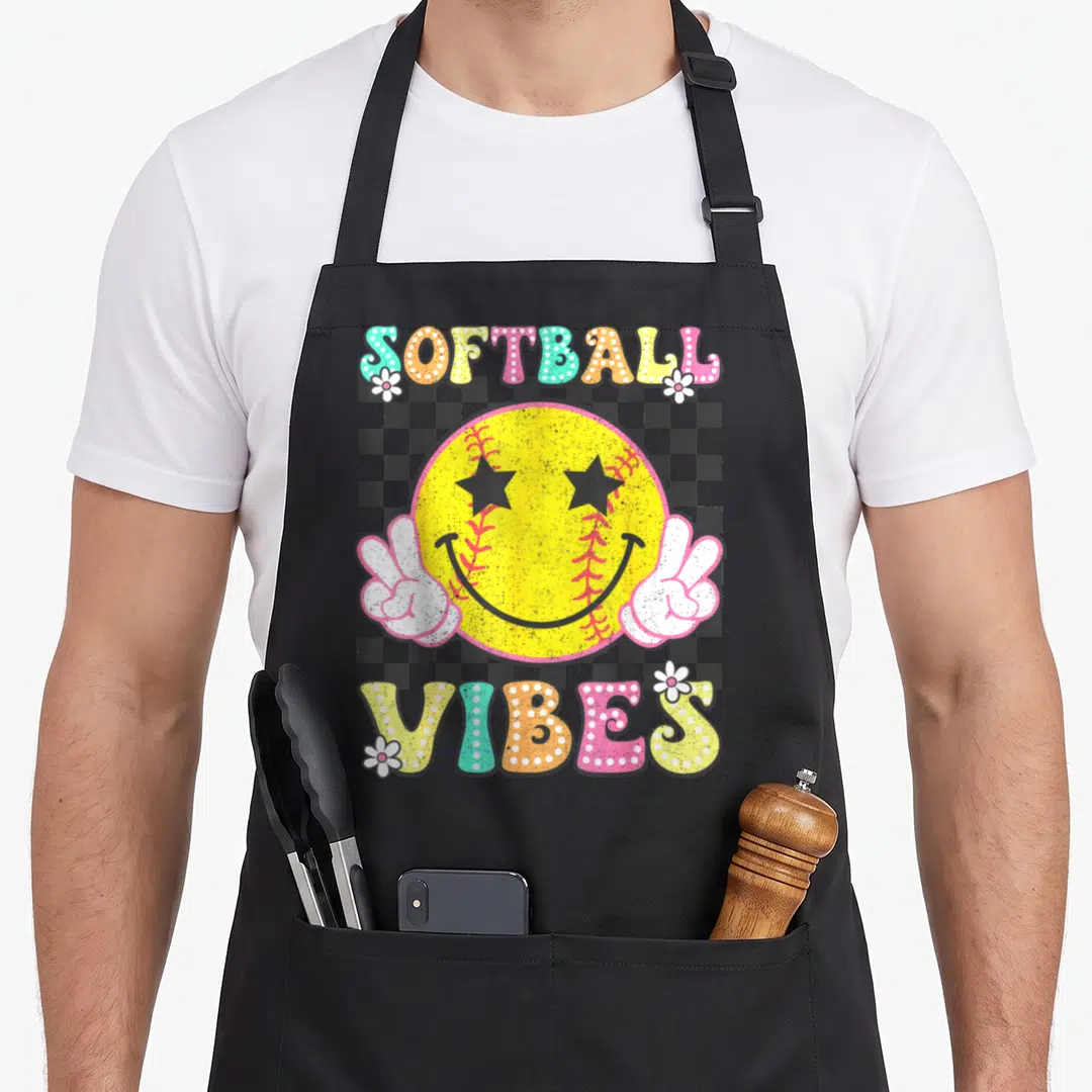 Softball game aprons - Retro smiley softball with peace hands and SOFTBALL VIBES text on checkerboard — shown on a black cotton canvas apron against a white background