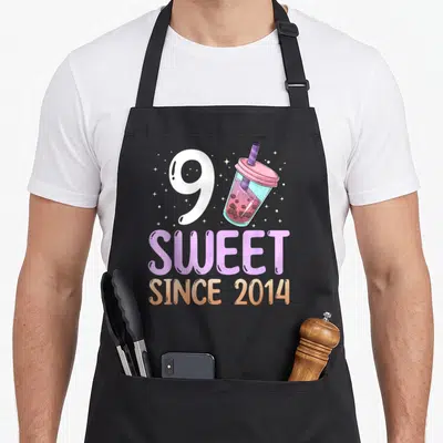 Bubble anime mom apron - White number 9 next to pink bubble tea cup with SWEET SINCE 2014 text — shown on a black cotton canvas apron against a white background