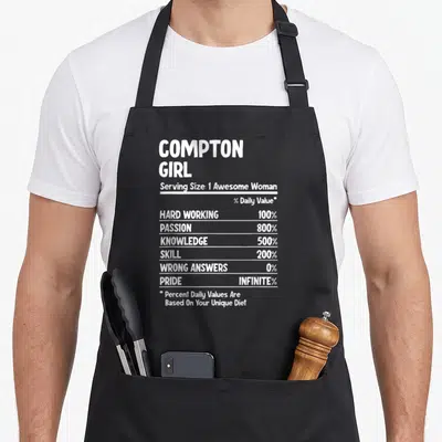 Funny compton apron - White nutrition facts label text on black apron reading Compton Girl with stats like 100% hard — shown on a black cotton canvas apron against a white background