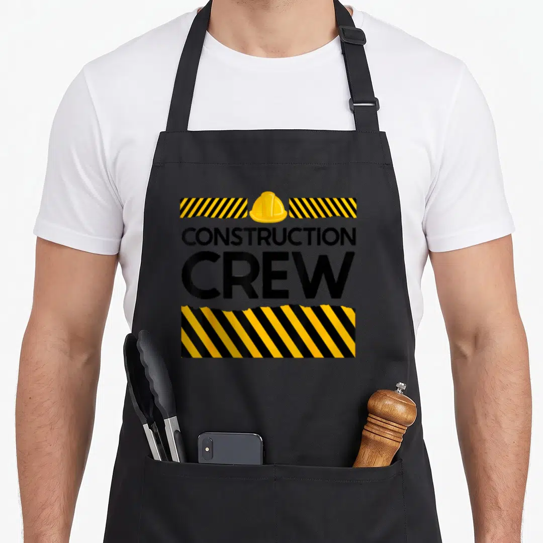 Crew construction apron - Yellow hard hat and CONSTRUCTION CREW text flanked by yellow and black striped bars — shown on a black cotton canvas apron against a white background
