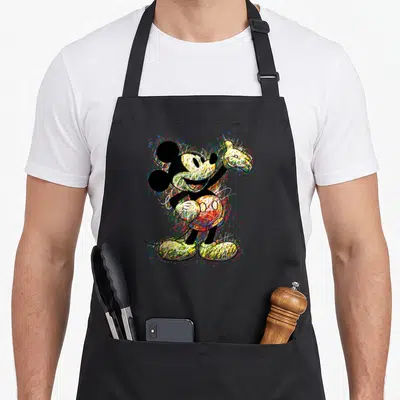 Scribble crazy mouse man apron - Mickey Mouse figure filled with red blue yellow green and black scribbles surrounded — shown on a black cotton canvas apron against a white background