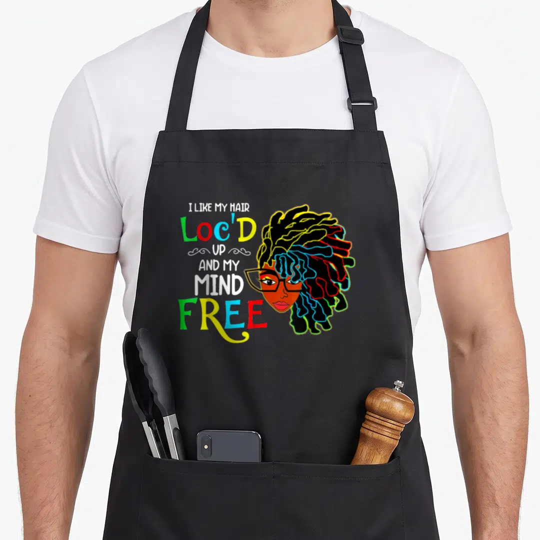 Locd hair apron - Cartoon woman with colorful locs next to stacked text I Like My Hair Loc'd Up and My Mind Free — shown on a black cotton canvas apron against a white background