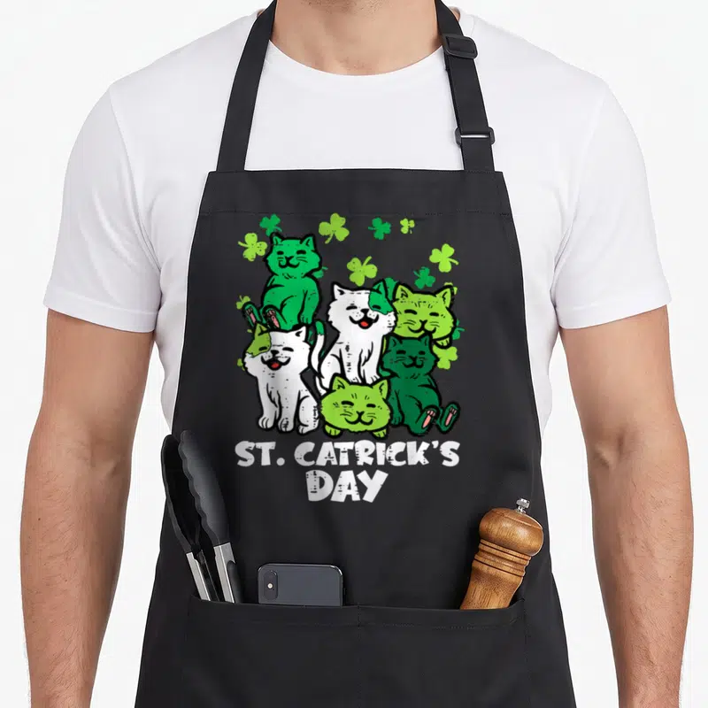 Catrick st patrick day aprons - Five cartoon cats and shamrocks above ST. CATRICK'S DAY text in green and white — shown on a black cotton canvas apron against a white background