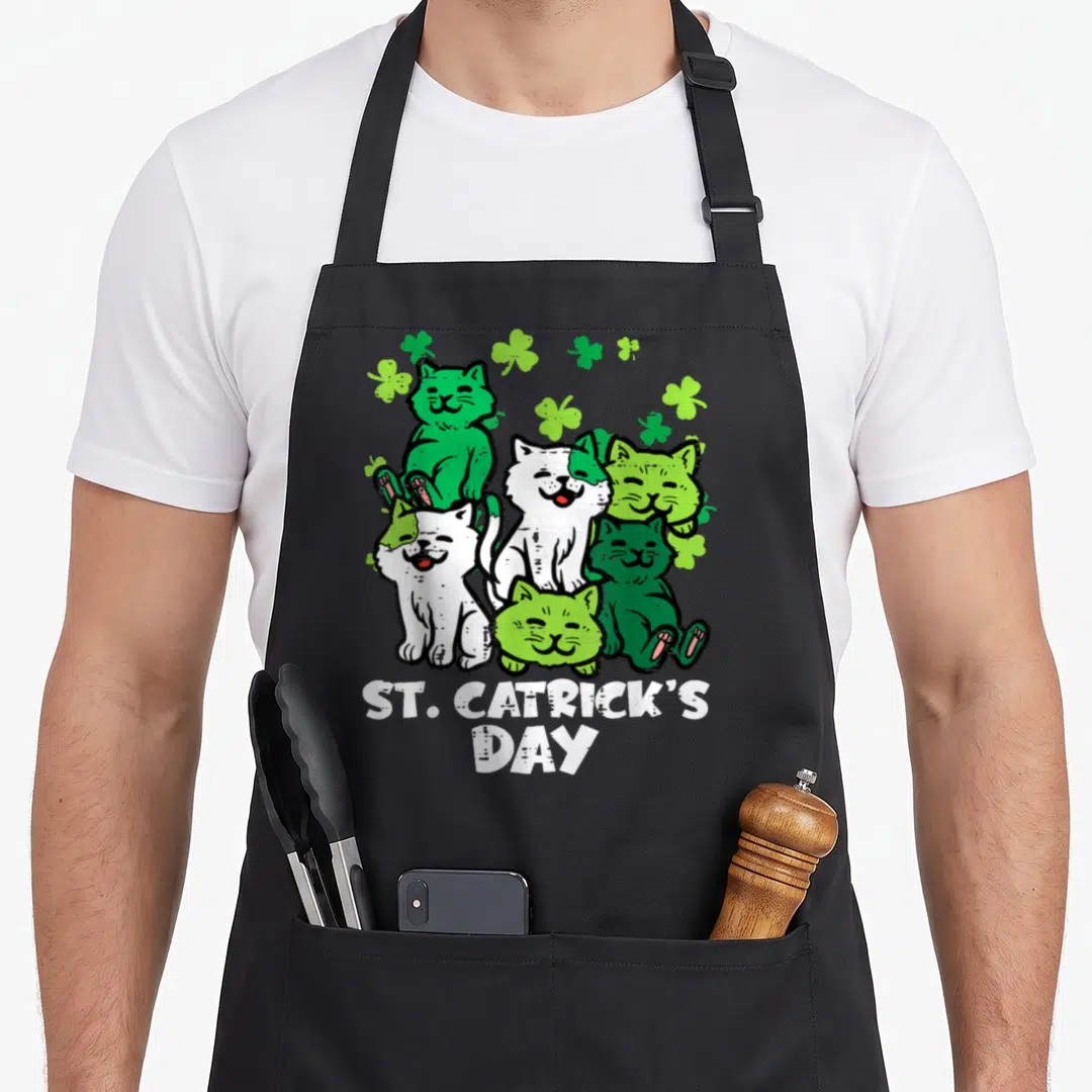 Catrick st patrick day aprons - Five cartoon cats and shamrocks above ST. CATRICK'S DAY text in green and white — shown on a black cotton canvas apron against a white background