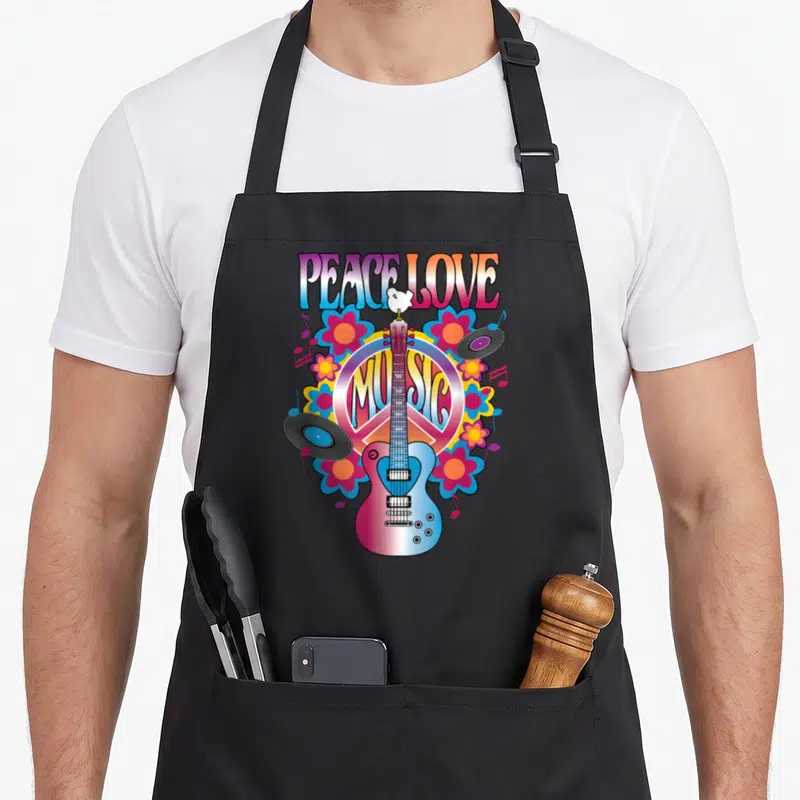 Peace vinyl apron - Cartoon guitar over peace sign with vinyl records, flowers, and PEACE LOVE MUSIC text — shown on a black cotton canvas apron against a white background