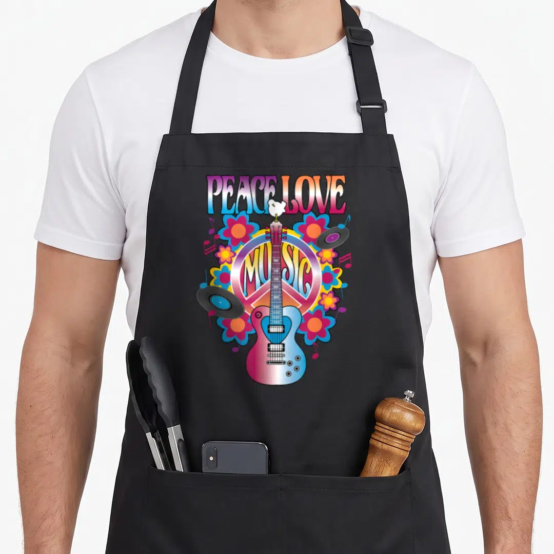 Peace vinyl apron - Cartoon guitar over peace sign with vinyl records, flowers, and PEACE LOVE MUSIC text — shown on a black cotton canvas apron against a white background