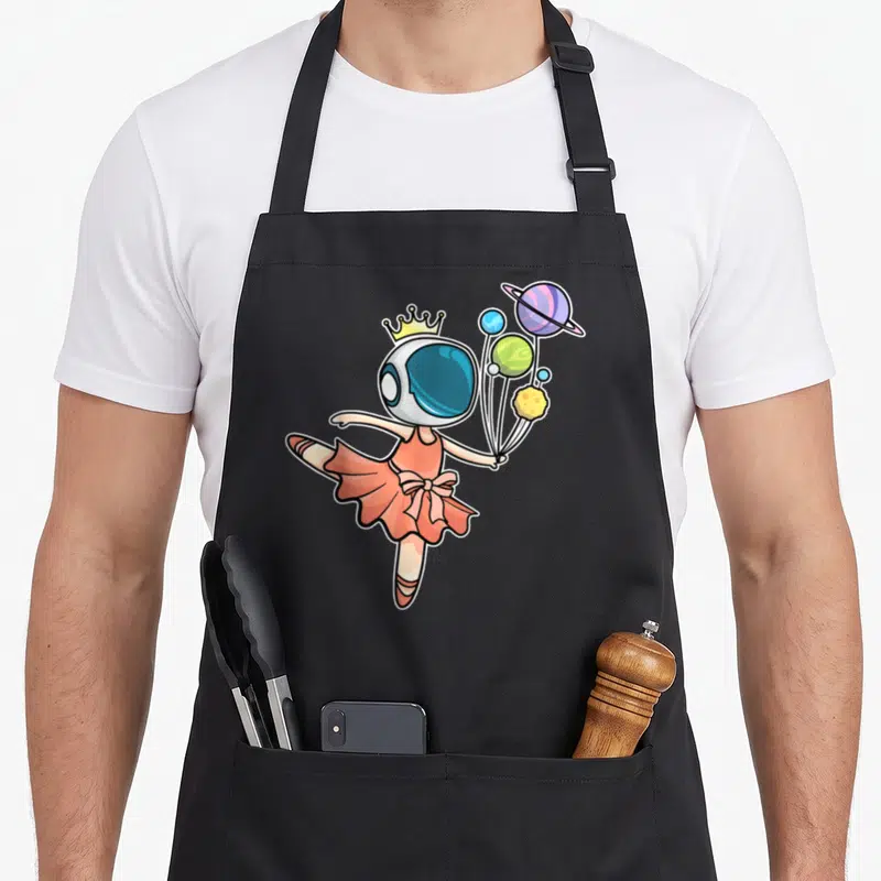 Space ballerina apron - Cartoon astronaut ballerina in peach tutu holding four colorful planets on strings — shown on a black cotton canvas apron against a white background