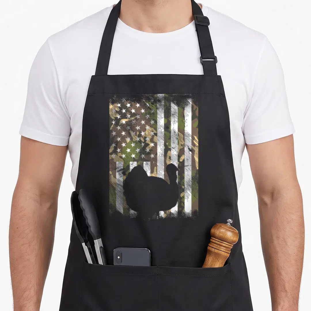Camo thanksgiving day aprons - Distressed camo USA flag background with centered grey turkey silhouette print — shown on a black cotton canvas apron against a white background