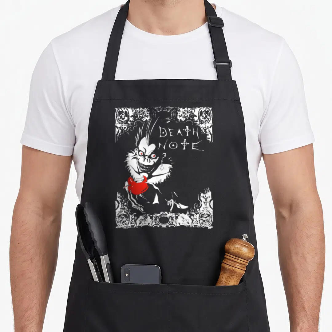 Ryuk apple apron - White line art Ryuk holding red apple next to Death Note text inside distressed border — shown on a black cotton canvas apron against a white background