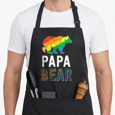 Lgbtq bear apron - Rainbow cartoon bear above white PAPA and outlined BEAR text — shown on a black cotton canvas apron against a white background