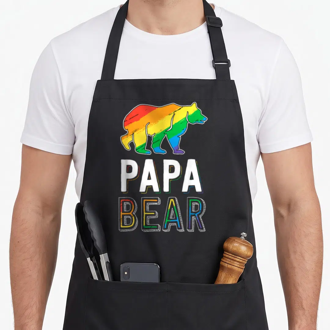 Lgbtq bear apron - Rainbow cartoon bear above white PAPA and outlined BEAR text — shown on a black cotton canvas apron against a white background