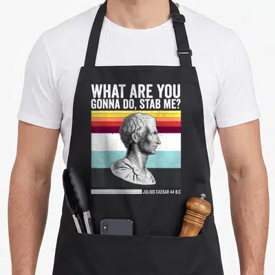 Stab caesar apron - Retro Julius Caesar bust over colorful stripes with sarcastic stabbing quote — shown on a black cotton canvas apron against a white background