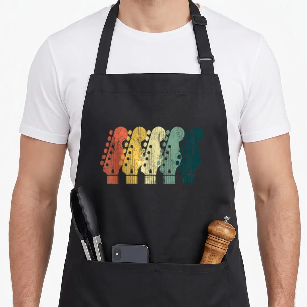 Guitar songwriter apron - Five retro guitar headstocks in orange yellow cream and green overlapping in a row — shown on a black cotton canvas apron against a white background