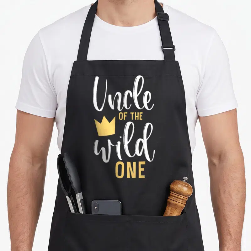 Uncle wild birthday apron - White and yellow Uncle OF THE wild ONE text with yellow crown graphic — shown on a black cotton canvas apron against a white background