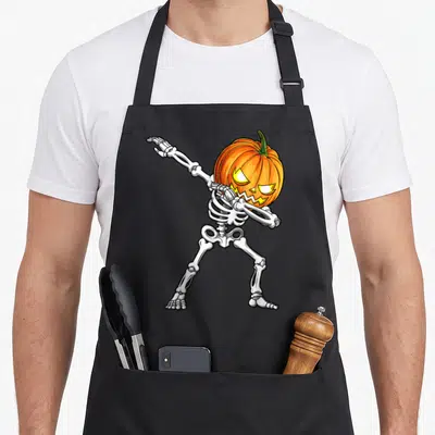 Skeleton scary halloween apron - Dabbing skeleton with glowing orange pumpkin head and white bones — shown on a black cotton canvas apron against a white background