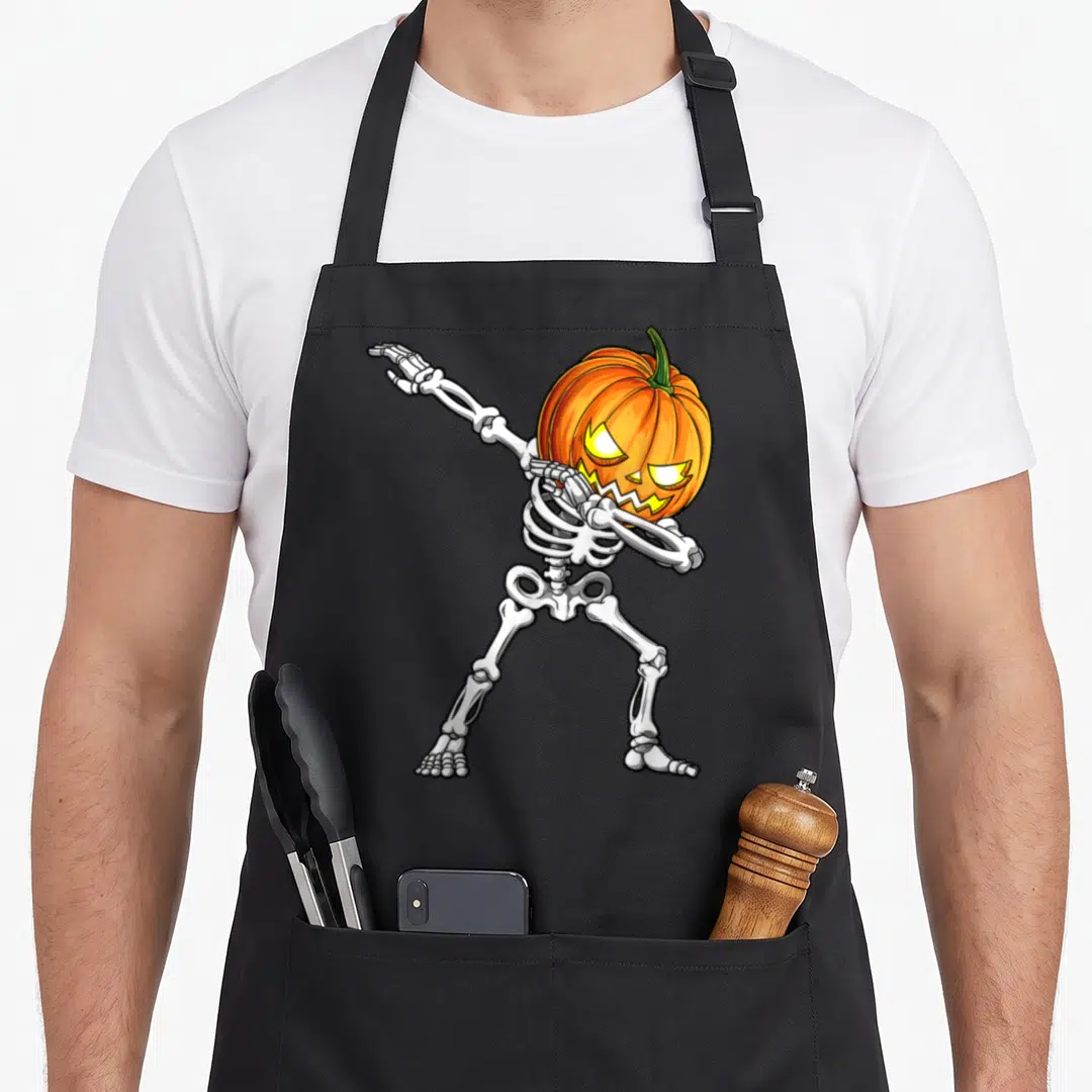 Skeleton scary halloween apron - Dabbing skeleton with glowing orange pumpkin head and white bones — shown on a black cotton canvas apron against a white background