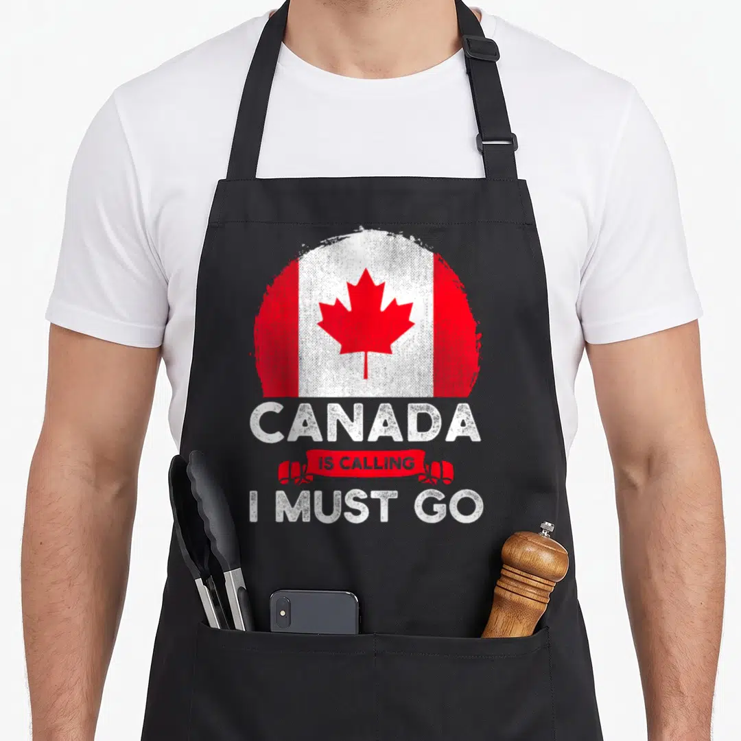 Calling canada aprons - Distressed circular Canadian flag with red ribbon text reading Canada Is Calling I Must Go — shown on a black cotton canvas apron against a white background