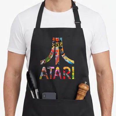 Atari colorful apron - Atari logo filled with Pong Asteroids game art in red yellow blue green — shown on a black cotton canvas apron against a white background