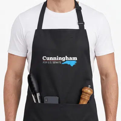 Cal senator apron - Cunningham FOR U.S. SENATE text with red line and light blue North Carolina map outline — shown on a black cotton canvas apron against a white background