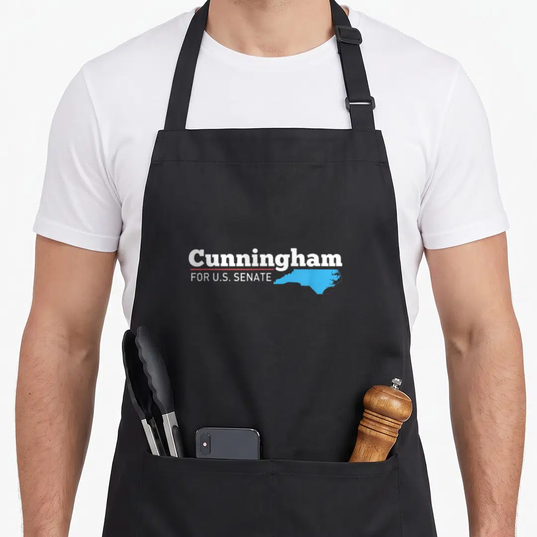 Cal senator apron - Cunningham FOR U.S. SENATE text with red line and light blue North Carolina map outline — shown on a black cotton canvas apron against a white background