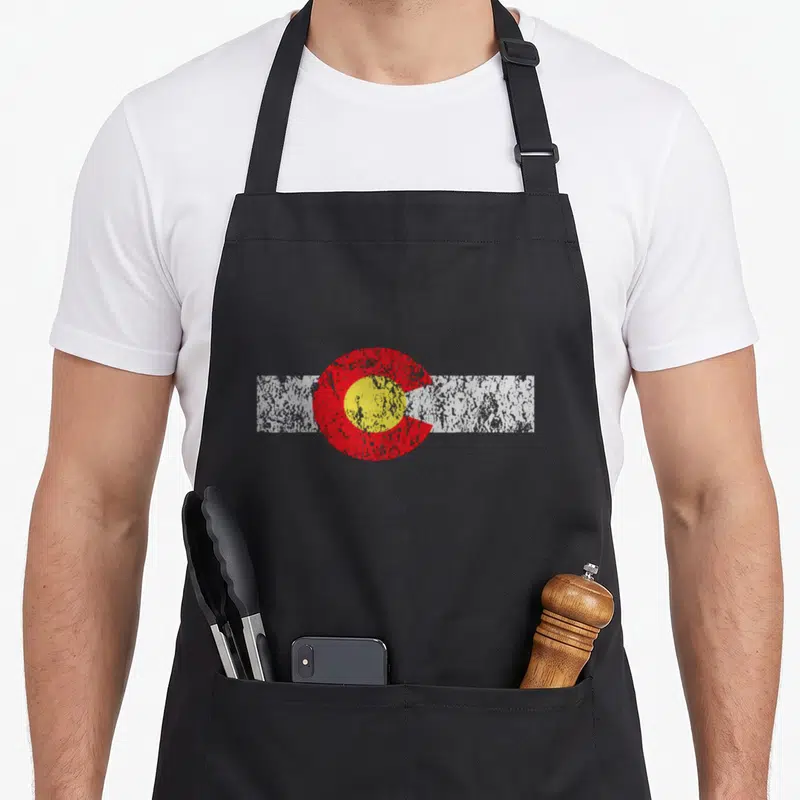 Distressed colorado apron - Red C shape with yellow circle over a white horizontal stripe — shown on a black cotton canvas apron against a white background