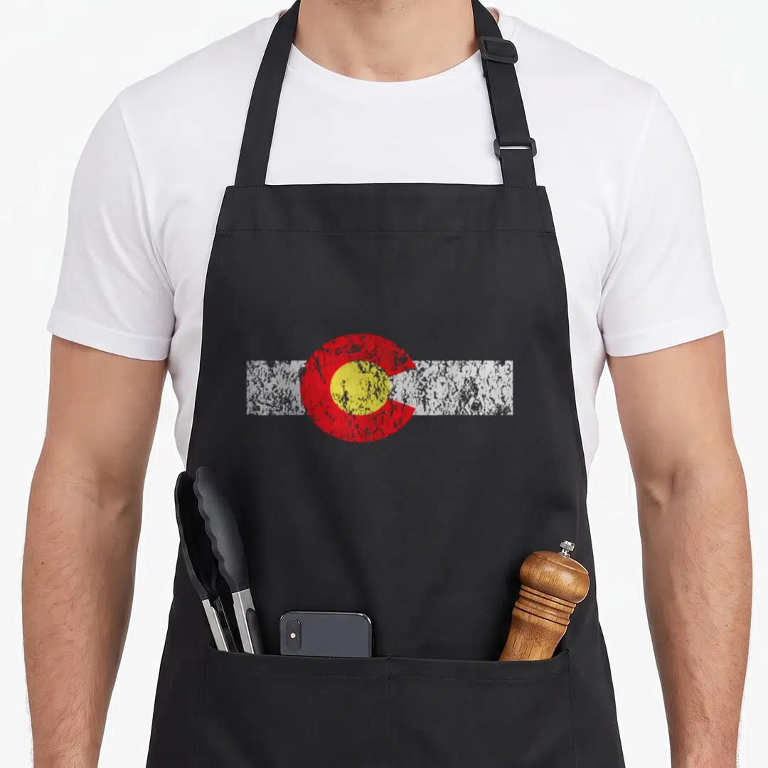 Distressed colorado apron - Red C shape with yellow circle over a white horizontal stripe — shown on a black cotton canvas apron against a white background