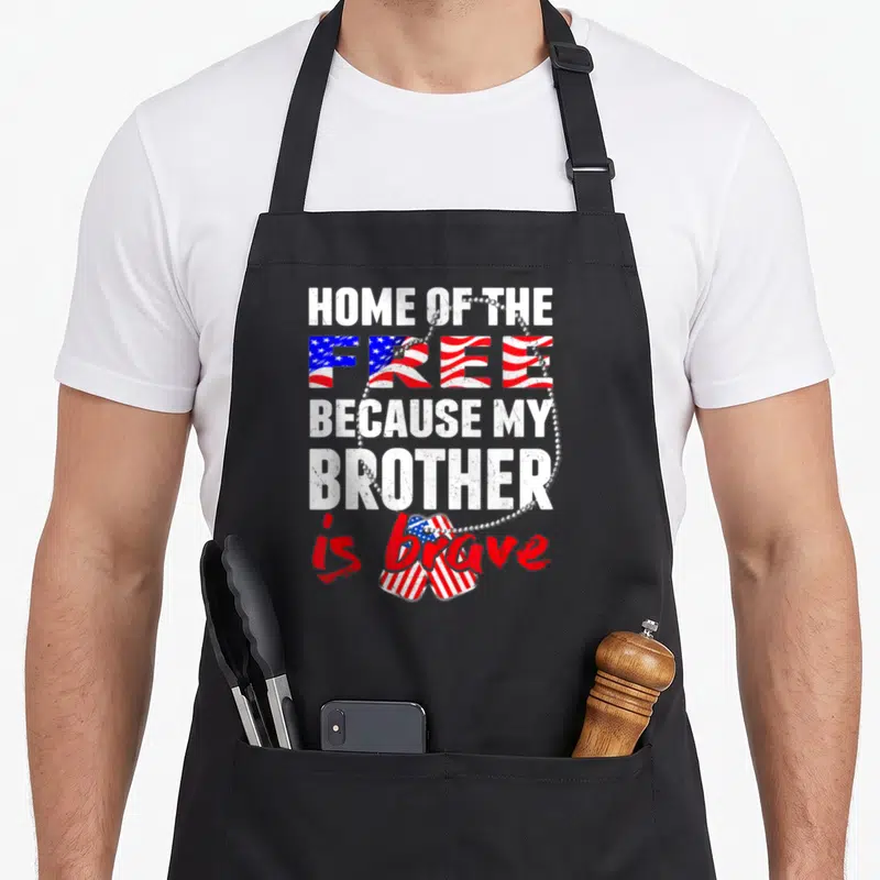 Brother grunt apron - Distressed text reading Home of the Free Because My Brother is brave with US flag heart and dog — shown on a black cotton canvas apron against a white background