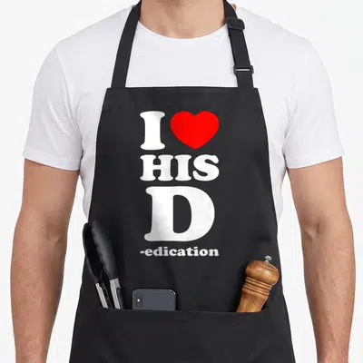 Dedication his hers aprons - Vertical white text I HIS D -edation with a red heart symbol replacing the word love — shown on a black cotton canvas apron against a white background