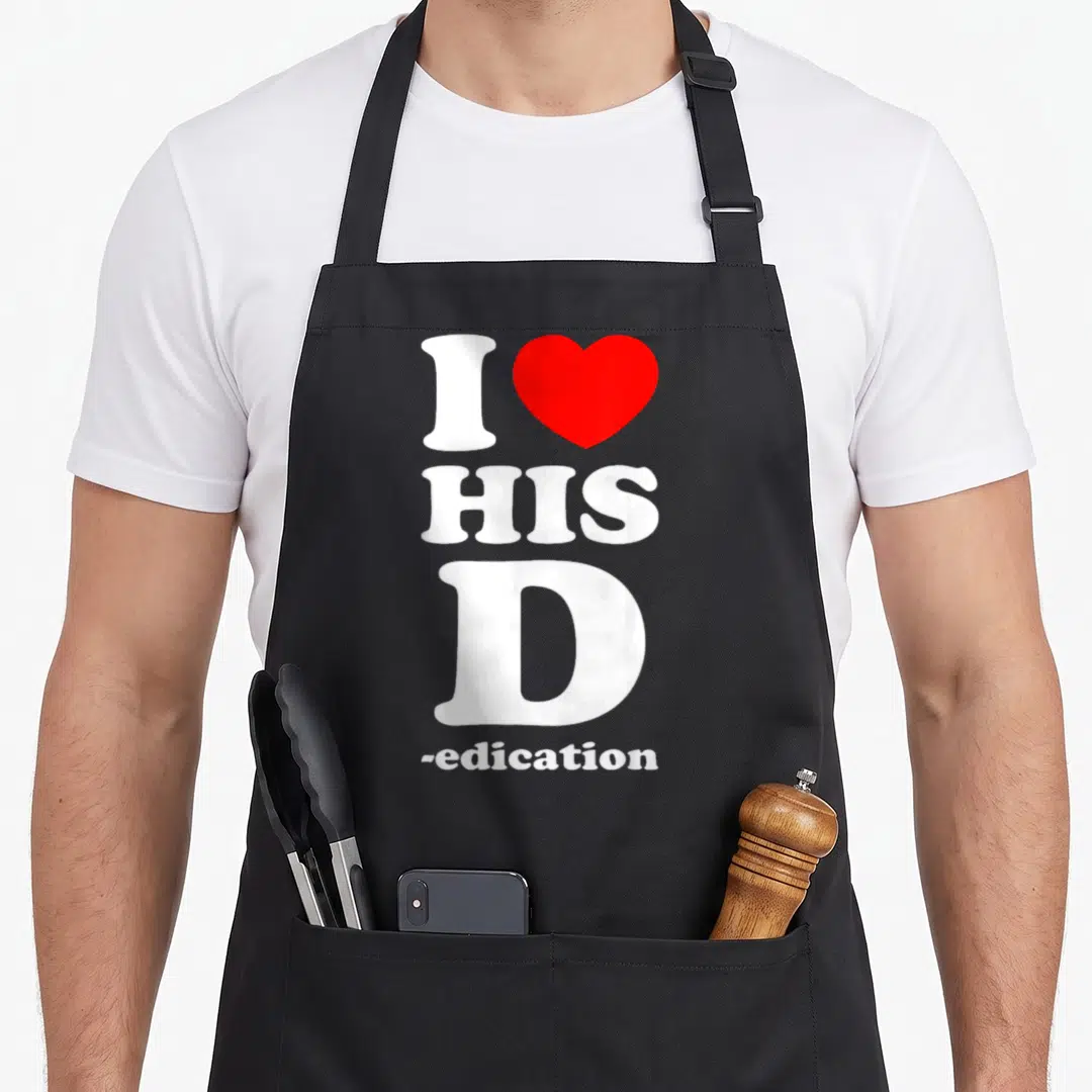 Dedication his hers aprons - Vertical white text I HIS D -edation with a red heart symbol replacing the word love — shown on a black cotton canvas apron against a white background