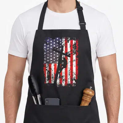 Lineman patriotic american flag apron - Grey lineman silhouette climbing pole over distressed red white and blue — shown on a black cotton canvas apron against a white background