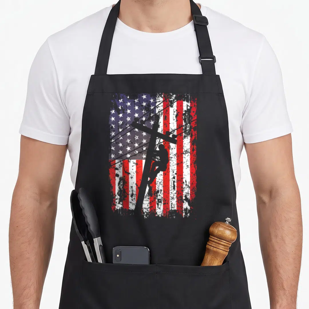 Lineman patriotic american flag apron - Grey lineman silhouette climbing pole over distressed red white and blue — shown on a black cotton canvas apron against a white background