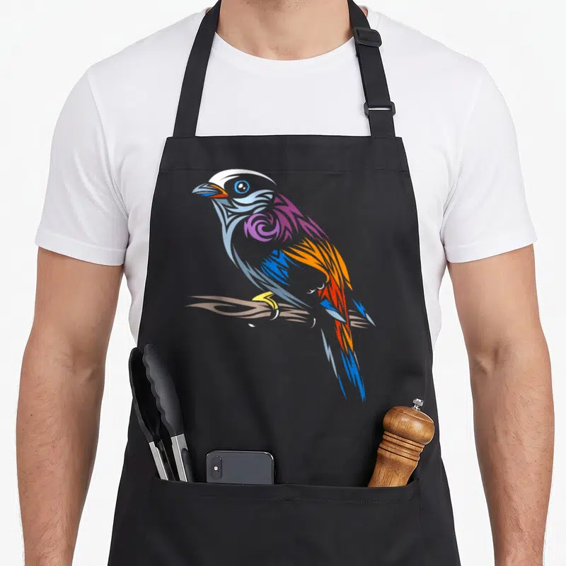Tribal bird apron - Stylized bird perched on branch with blue purple orange red and brown geometric patterns — shown on a black cotton canvas apron against a white background