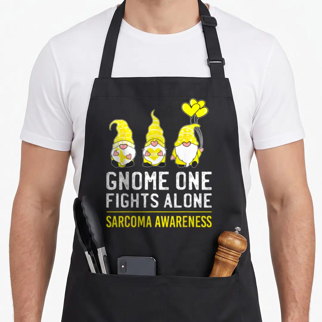 Fight alone ribbon apron - Three yellow gnomes holding balloons above white and yellow text reading GNOME ONE FIGHTS — shown on a black cotton canvas apron against a white background